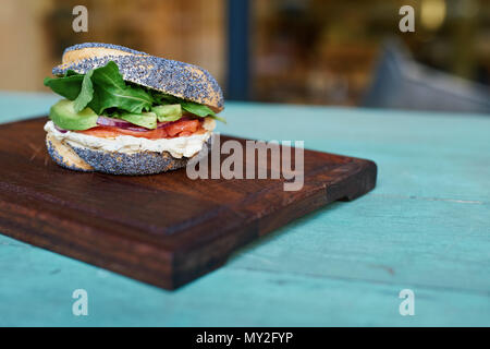 Lecker Lachs und Frischkäse Mohn Bagel mit Gemüse ruht auf einer Platine auf einem urigen türkis Holztisch Stockfoto