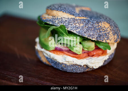 Nahaufnahme von einem leckeren Lachs und Frischkäse Mohn Bagel mit Gemüse Sitzen auf einem hölzernen mit Board Stockfoto