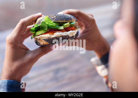 Mann stand draußen zu einem leckeren Lachs und Frischkäse Mohn Bagel essen hält er Stockfoto