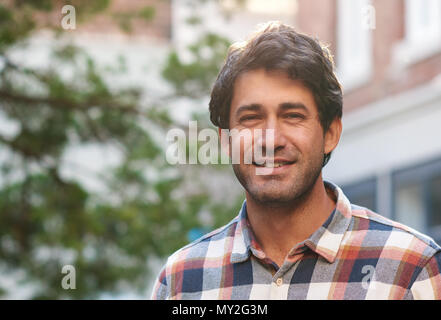 Closeup Portrait von einem lässig gekleidet, stattlicher Mann lächelnd, während sie von sich selbst stehend auf einer Straße in der Stadt an einem sonnigen Nachmittag Stockfoto