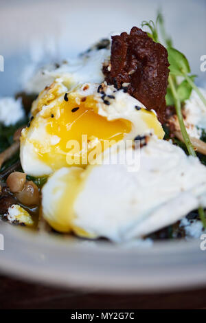 Zwei pochierte Eier mit flüssig Eigelb in einer Schüssel mit lecker gebratene Pilze, Feta und gemischter Salat auf einem Tisch Stockfoto