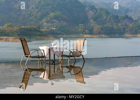 Tisch und Stühle im Wasser im Infinity-Pool mit Blick auf den See und die Berge Landschaft wider Stockfoto