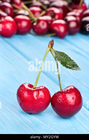 Zwei rote Kirschen mit Tropfen auf dem Tisch vor dem Hintergrund der zerstreuten Beeren Stockfoto