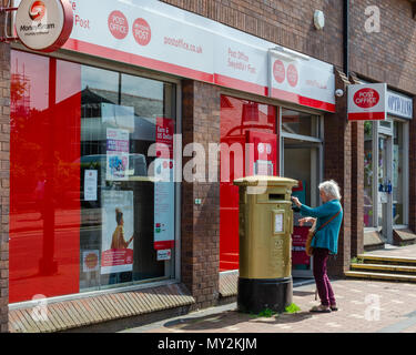 Feuerstein, UK: Juni 4, 2018: Eine ältere Frau Beiträge einige Briefe in der Post Box außerhalb Feuerstein Post. Stockfoto