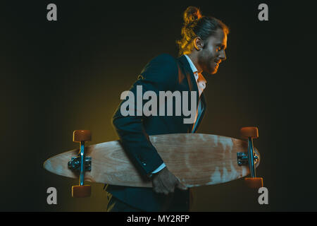 Seitenansicht der jungen kaukasischen Mann im Smoking und Holding skateboard Stockfoto