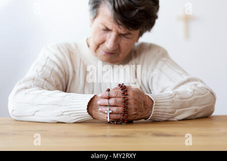 Religiöse senior betende Frau mit roten Rosenkranz in der Kirche. Konzentrieren Sie sich auf die Hände Stockfoto