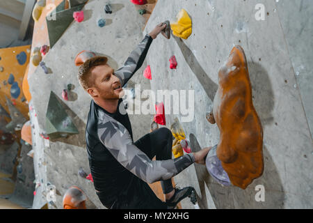 Junger Mann in sportliche Kleidung klettern eine Wand mit Griffe am Gym Stockfoto