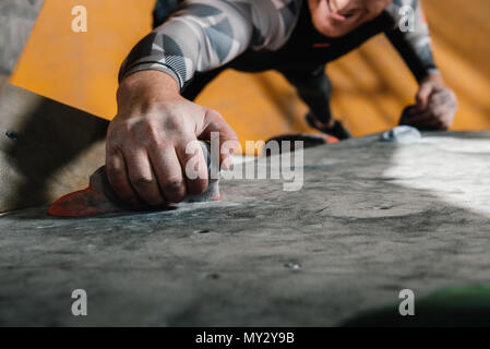 7/8 Schuß des jungen Mannes in sportliche Kleidung klettern eine Wand mit Griffe am Gym Stockfoto