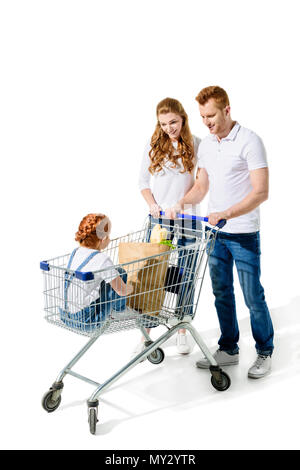 Glückliche junge Eltern auf der Suche nach süßen kleinen Tochter in Warenkorb sitzt isoliert auf weißem Stockfoto