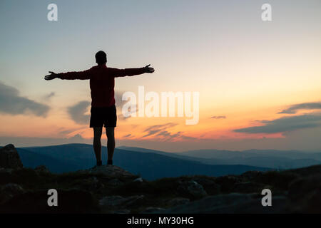 Mann feiern Sonnenuntergang am Berg. Auf inspirierende Aussicht. Trail Runner, Wanderer oder Bergsteiger erreicht Gipfel, geniessen Sie inspirierende Landschaft Stockfoto