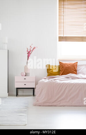 Real Photo eines weiblichen Schlafzimmer Innenraum mit Pink Sheets auf einem Bett steht in der Nähe der Fenster und hölzernen Nachttisch mit Blumen Stockfoto