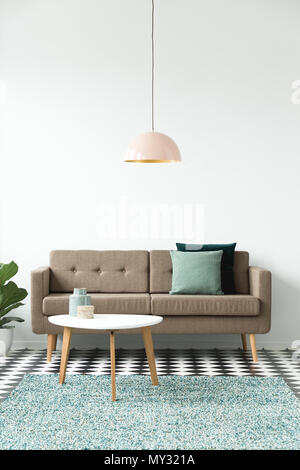 Vorderansicht eines Sofa mit Kissen, Couchtisch, Kronleuchter und grünen Teppich auf einer weißen Wand im Wohnzimmer Innenraum Stockfoto