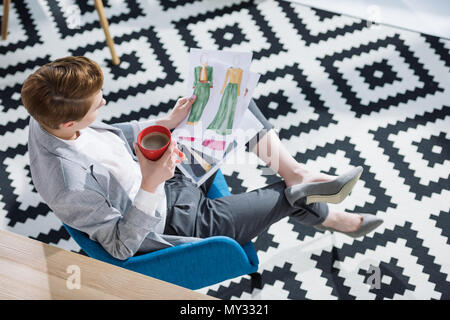 Hohe Betrachtungswinkel von Young Fashion Designer mit Tasse Kaffee auf Skizzen auf der Suche Stockfoto