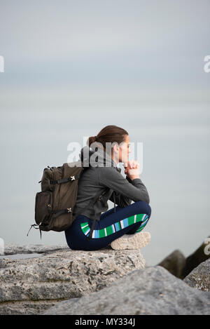 Frau trägt einen Rucksack sitzen auf den Felsen ruhen und genießen die Aussicht Stockfoto