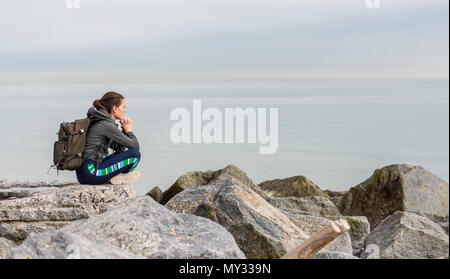 Frau trägt einen Rucksack sitzen auf den Felsen ruhen und genießen die Aussicht Stockfoto