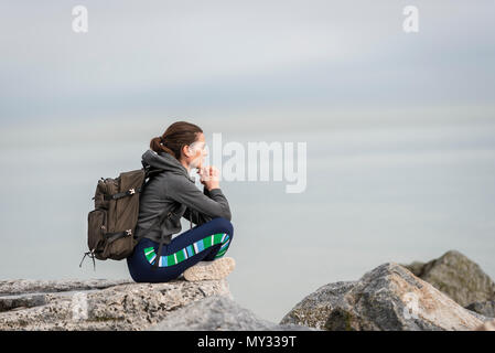 Frau trägt einen Rucksack sitzen auf den Felsen ruhen und genießen die Aussicht Stockfoto