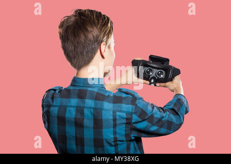Rückansicht des jungen Mannes holding VR-Headset. studio Shot, auf rosa Hintergrund isoliert. Stockfoto