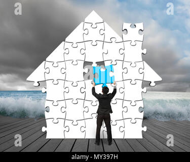 Mit einem blauen Puzzle im Haus Form auf hölzernen Pier mit bewölkt und Welle Stockfoto