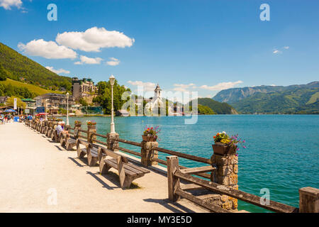 St. Wolfgang, Österreich - 27. Mai 2017: Uferpromenade auf alpinen Wolfgangsee mit einer Reihe von holzbänken. Blick auf St. Wolfgang Kirche und Mo Stockfoto