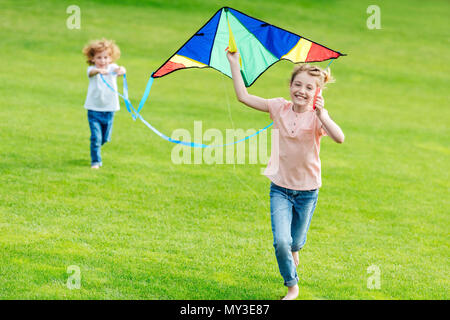 Gerne nette Geschwister spielen mit Kite während der Ausführung auf grünem Rasen im Park Stockfoto