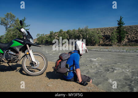 Motorrad reisenden Mann auf extreme Bank von Whitewater river stream in der Nähe des Motorrads im Altai Gebirge Sibirien Russland sitzen Stockfoto