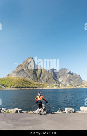 Eine weibliche Radfahrer genießt die Aussicht auf den Fjord an Reine, Lofoten, Norwegen. Stockfoto