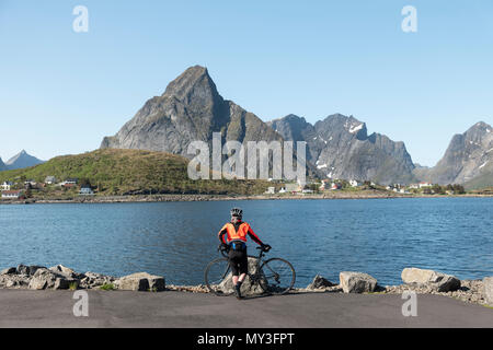 Eine weibliche Radfahrer genießt die Aussicht auf den Fjord an Reine, Lofoten, Norwegen. Stockfoto