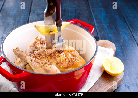 Einen gusseisernen Topf und ein goldenes Huhn mit Zitrone und Rosmarin aus dem Ofen. Köstliches Abendessen mit der Familie. Für Text setzen. Kopieren Sie Platz Stockfoto