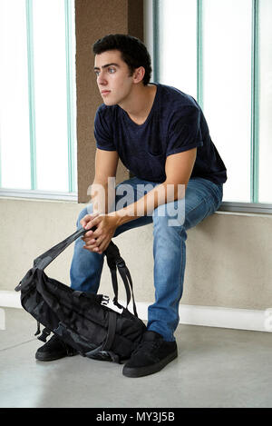 Junge Mann in der Schule Flur sitzen, Porträt Stockfoto