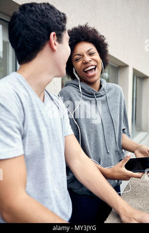 Junge Frau lachend während der Wiedergabe Ohrhörer mit Freund Stockfoto