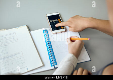 Studenten mit Smartphone Taschenrechnerfunktion beim Durchführen der Mathematik Zuordnung Stockfoto