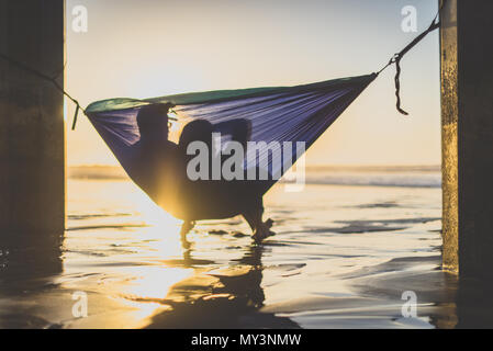 Silhouette von Paar den Sonnenuntergang am Strand in der Hängematte Stockfoto