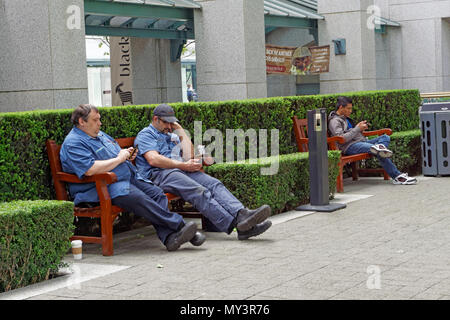 Männer auf Benches mit Handys in Vancouver, BC, Kanada sitzen Stockfoto