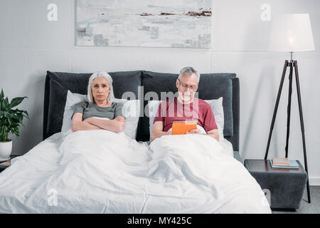 Mann mit Tablette während mürrische Ehefrau in der Nähe von im Bett liegend Stockfoto