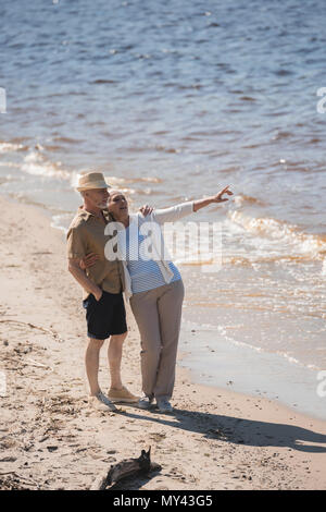 Gerne älteres Paar ständigen umarmen am Sandstrand und Wegsehen Stockfoto