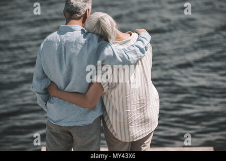 Rückansicht des älteren Paares ständigen umarmen und mit Blick auf die Wellen Stockfoto