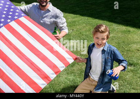 Vater und Sohn auf Gras mit uns sitzen Flagge und halten Getränke, Amerikas Unabhängigkeitstag Konzept Stockfoto