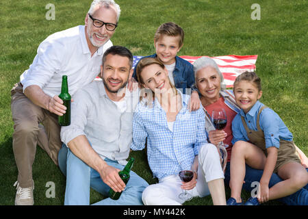 Glückliche Familie von drei Generationen zusammen sitzen auf grünen Rasen und lächelnd an Kamera Stockfoto