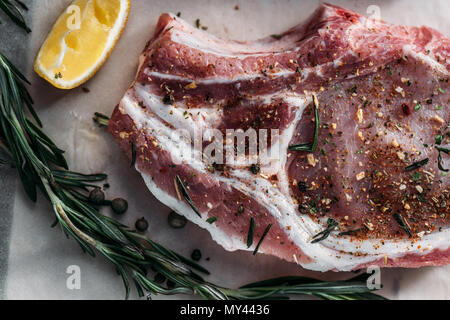 Nahaufnahme Blick auf raw ribeye Steak mit Gewürzen, Zitrone und Rosmarin auf Backpapier Stockfoto