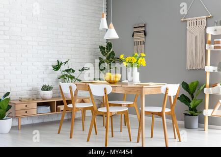 Weiße Lampen über Holz- Tisch und Stühle im Speisesaal Interieur mit gelben Blumen. Real Photo Stockfoto