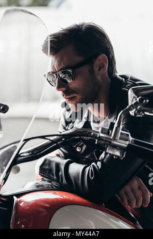 Close-up Portrait von Stattlichen stilvolle junger Mann in Sonnenbrille und Lederjacke sitzen auf dem Motorrad Stockfoto