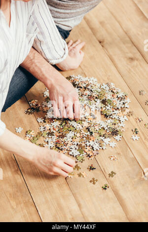 7/8 Schuß des jungen Paares sammeln Puzzle auf Holzboden Stockfoto