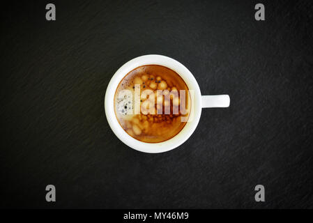 Espresso in der kleinen weißen Schale auf schwarzem Schiefer Hintergrund, Ansicht von oben Stockfoto