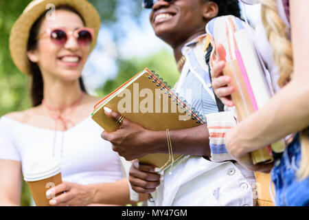 Fröhlicher junger multiethnischen Studierende mit Bücher und Reden in Park Stockfoto