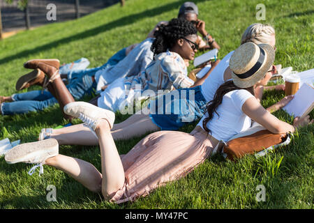 Jungen multiethnischen Studenten lesen Bücher beim Liegen auf Gras und Studieren in Park Stockfoto