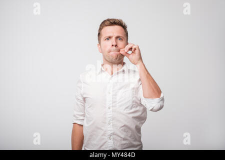 Portrait von gutaussehenden jungen Mann im weißen Hemd seinen Mund schließen, s er gezwungen ist, geheim zu halten, nicht jedermann zu erzählen. Stockfoto