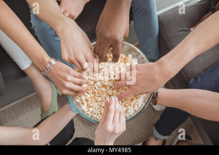 Blick von oben auf die weiblichen und männlichen Händen die Popcorn aus dem Abscheidegefäß Stockfoto