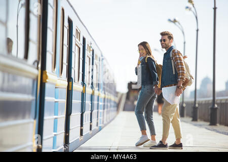 Paar stilvolle Reisende in der Sonnenbrille mit Karte und Rucksäcken warten in Zug bei der U-Bahn Station zu kommen Stockfoto