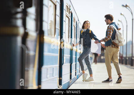 Paar stilvolle Touristen mit Rucksäcken und Karte, die in der Bahn am U-Bahnhof im Freien Stockfoto