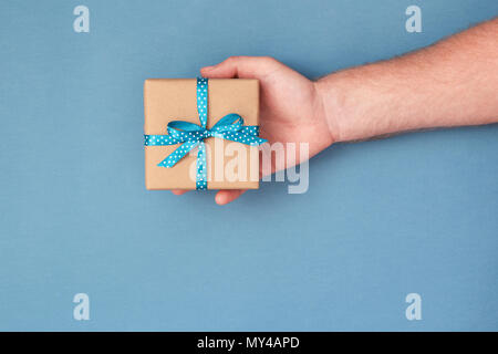 Der Mann hält Kraftpapier Geschenkbox mit Schleife gebunden. Ansicht von oben, urlaub Konzept. Stockfoto